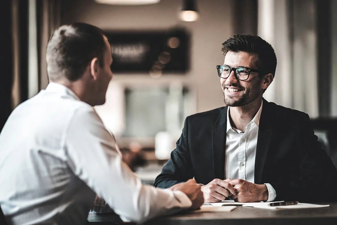 Two businessmen in formal attire smiling during a professional meeting at a table